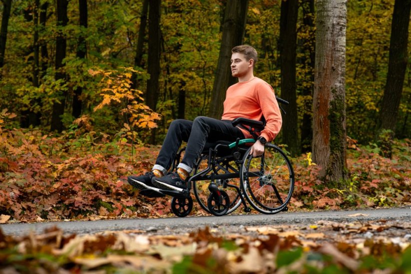 Invalidní vozík ACTIV-TIM v přírodě, uživatel na lesní cestě, lehký model vhodný pro venkovní použití