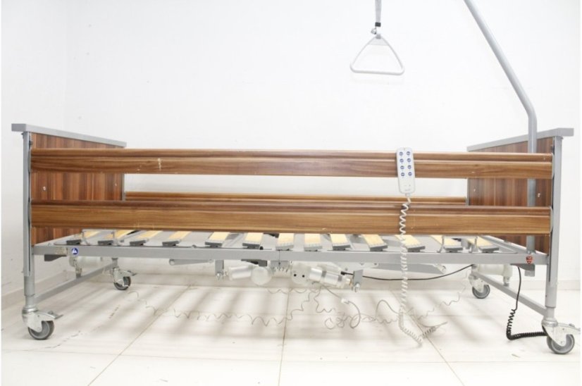 Polohovací postel Domiflex II s bezpečnostními bočnicemi ve vztyčené poloze, tmavé dřevěné obložení, elektrické ovládání